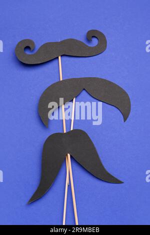 Bâtons en bois avec différentes moustaches en papier sur fond bleu Banque D'Images