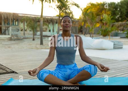 Heureuse femme afro-américaine pratiquant la méditation de yoga assise sur la plage ensoleillée Banque D'Images