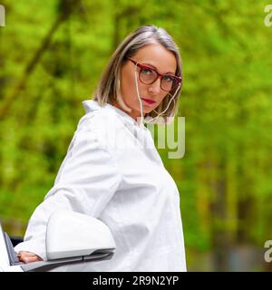 Femme portant une chemise blanche et regardant directement sur le fond vert luxuriant Banque D'Images