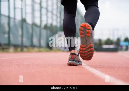 Sportsman dans des baskets confortables qui s'exécutent le long d'une piste caoutchoutée rouge sur un terrain urbain Banque D'Images