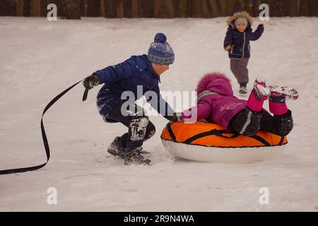 Les enfants montent en hiver à partir d'une glissade de glace sur un tubing multicolore. Bébé souriant et heureux avec tube de neige, glissant sur la pente de neige. Banque D'Images