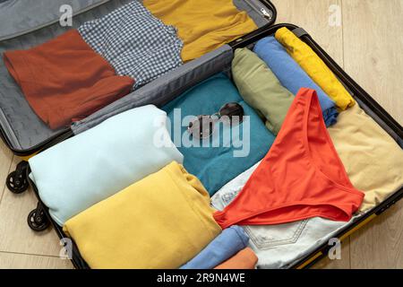 Vue en haut d'une valise préparée pour des vacances en bord de mer. Vêtements soigneusement pliés, maillot de bain rouge et lunettes de soleil. Le concept d'un séjour sûr en mer Banque D'Images