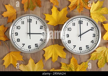 Deux horloges, l'une montre trois heures, l'autre deux heures. Des feuilles jaunes d'automne tombées sont autour. Symbole de changement d'heure par rapport à l'heure d'été Banque D'Images