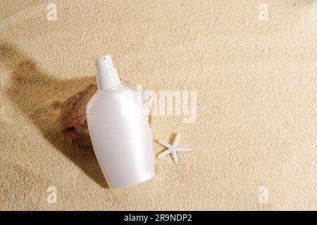 Crème solaire ou cosmétique pour le corps en bouteille blanche restant près de la pierre sur fond de sable . Écran solaire avec protection UVA et UVB. Été, mer Banque D'Images