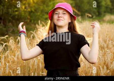 Une adolescente joyeuse, âgée de 12 ou 13 ans, se tient avec élégance dans un arrière-plan d'été jaune vif. Pour compléter son look, c'est un élégant chapeau Panama. Des mains à Banque D'Images