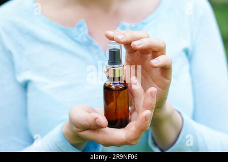 Femme en tissu bleu tenant une bouteille de verre brun avec de l'huile cosmétique spa. salon de thérapie, produits naturels de soins du corps écologiques Banque D'Images