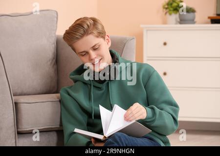 Un adolescent lit le livre près d'un fauteuil dans la chambre Banque D'Images