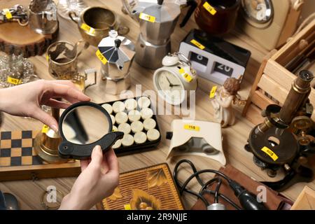 Femme tenant la loupe près de la table avec différentes choses, au-dessus de la vue. Vente de garage Banque D'Images