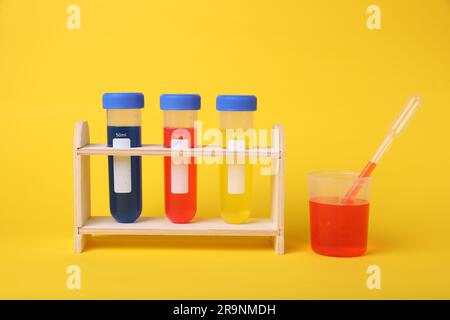 Bécher et tubes à essai avec liquides colorés sur support en bois sur fond jaune. Kit d'expérimentation chimique pour enfants Banque D'Images
