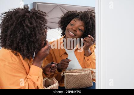 Bonne femme africaine appliquant la mascara devant le miroir. Banque D'Images