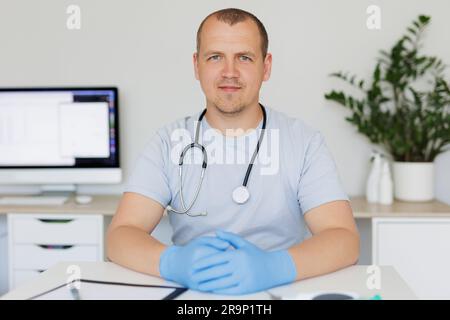 Portrait d'un médecin souriant portant un uniforme médical assis à la table de l'hôpital Banque D'Images