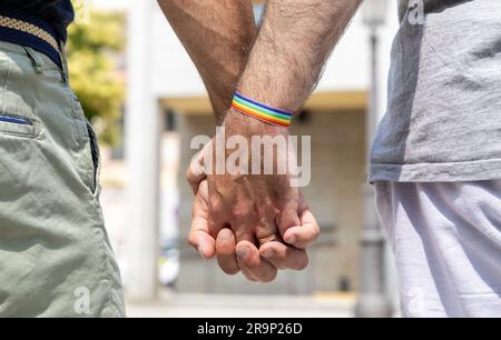 Gros plan d'un couple gay masculin tenant les mains avec un bracelet arc-en-ciel sur un poignet. Concept de fierté gay Banque D'Images