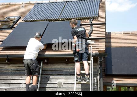 Deux techniciens installant des panneaux Perlite 410kW noirs sur un toit en tuiles qui possède déjà un jeu de tubes et sous vide pour le chauffage solaire de l'eau à Coleman Banque D'Images