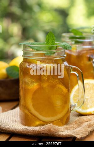 Thé glacé dans des pots en verre avec des tranches de citron et menthe dehors sur table en bois avec fond de nature Banque D'Images