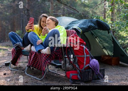 Maman et fille pendant un appel vidéo en ligne. Ils s'assoient dans des chaises pliantes près de la tente et communiquent avec leur père par liaison vidéo. Maternité et confiance o Banque D'Images