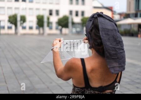 Kaiserslautern, Allemagne. 28th juin 2023. Artiste féminine regardant le modèle d'esquisse transparent. Onze artistes internationaux de 6 pays transforment le pavé Stiftsplatz (place) en art tridimensionnel. 3D l'art de la rue utilise la perspective pour créer l'illusion optique de l'espace. Les visiteurs sont invités à observer tous les artistes au travail pendant trois jours, du mercredi à 8 h 00 au vendredi à 6 h 00. Cette année, le sujet est « Digitalisation et Smart City ». Les tableaux illustrent des robots, des données ou des scénarios de cyberpunk. Credit: Gustav Zygmund/Alamy News Banque D'Images