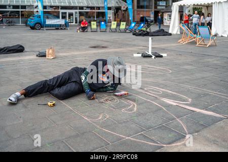 Kaiserslautern, Allemagne. 28th juin 2023. Artiste peignant dans une position plus confortable. Onze artistes internationaux de 6 pays transforment le pavé Stiftsplatz (place) en art tridimensionnel. 3D l'art de la rue utilise la perspective pour créer l'illusion optique de l'espace. Les visiteurs sont invités à observer tous les artistes au travail pendant trois jours, du mercredi à 8 h 00 au vendredi à 6 h 00. Cette année, le sujet est « Digitalisation et Smart City ». Les tableaux illustrent des robots, des données ou des scénarios de cyberpunk. Credit: Gustav Zygmund/Alamy News Banque D'Images