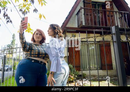 Deux jeunes femmes Latina élégantes, amies d'origine Argentine, se tiennent à l'extérieur de leur maison à midi dans un quartier de la province de Buenos Aires Banque D'Images