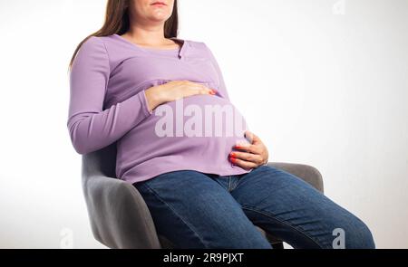 Une fille enceinte s'assoit sur une chaise au travail, sur fond blanc. La notion de congé de maternité et de conditions de travail en vertu de la loi. Avantages et ma Banque D'Images