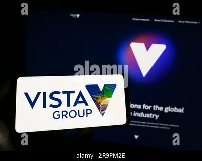 Personne tenant un smartphone avec le logo de la société Vista Group International Limited à l'écran devant le site Web. Mise au point sur l'affichage du téléphone. Banque D'Images