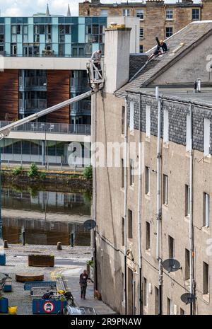 Des ouvriers de préparateur de cerisier remplaçant l'évent de toit par un homme marchant en dessous, Leith, Édimbourg, Écosse, Royaume-Uni Banque D'Images