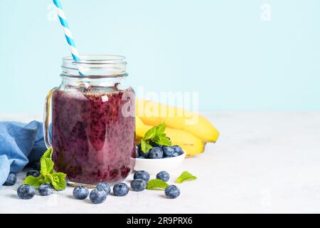 Smoothie à la banane aux myrtilles dans un pot en verre sur fond bleu. Banque D'Images