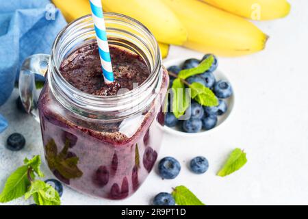 Smoothie à la banane aux myrtilles dans un pot en verre sur fond bleu. Banque D'Images