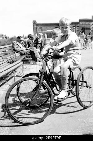 Archive historique année 1950 vue de la location de vélos de bord de mer terrain de jeu où trois cycles de roues de pédale ont été prêtés à de jeunes vacanciers avec ce garçon de huit ans devant cette image la seule personne couverte par un modèle de libération à la ville de bord de mer de Rhyl d'après-guerre dans Denbighshire Nord-Galles du Royaume-Uni. Remarque : aucune autre autorisation de modèle ou de propriété n'est disponible. Banque D'Images