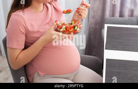 Une fille enceinte avec un gros ventre s'assoit dans la cuisine et mange une salade de vitamines végétales. Une alimentation adéquate pendant la grossesse. Régime alimentaire Banque D'Images