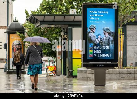 Bannière publicitaire informant sur le prochain sommet de l'OTAN 2023 dans le centre de Vilnius, capitale de la Lituanie, avec une femme avec parapluie marchant à proximité Banque D'Images