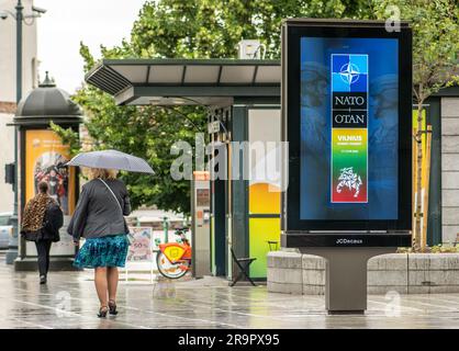 Bannière publicitaire informant sur le prochain sommet de l'OTAN 2023 dans le centre de Vilnius, capitale de la Lituanie, avec une femme avec parapluie marchant à proximité Banque D'Images