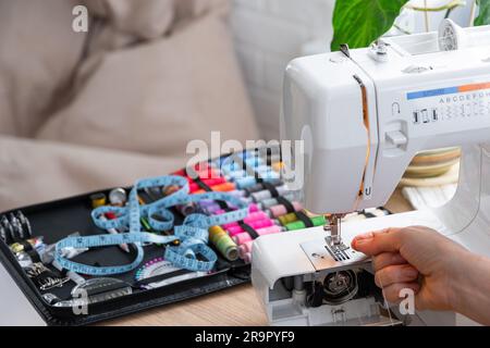 Femme main gros plan des ragoûts tulle sur machine à coudre électrique. Remplissage du fil dans l'aiguille de couture, réglage de la tension. Confort dans la maison, a h Banque D'Images