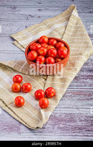 Un bol de tomates cerises mûres sur une nappe brune. Banque D'Images