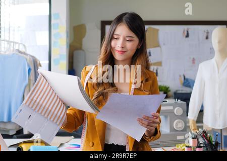 Femme designer de mode femme travaillant sur ses dessins dans atelier studio, femme propriétaire d'affaires avec des vêtements, tailleur propriétaire d'affaires, magasin de vêtements Banque D'Images