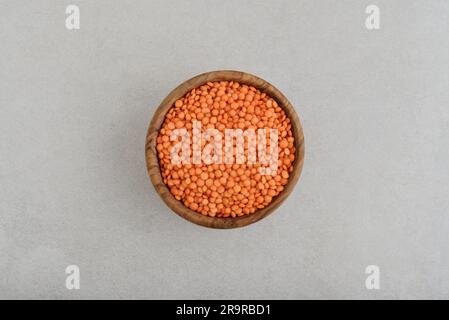 Lentilles rouges biologiques sèches dans un bol en bois sur fond de béton, vue de dessus Banque D'Images