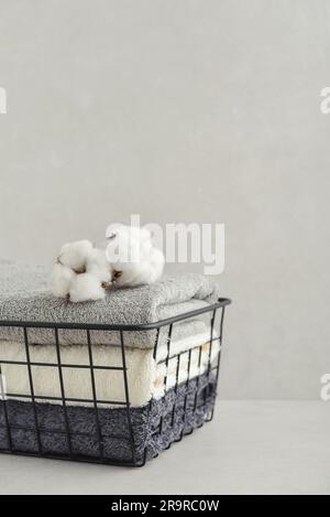 Pile de serviettes de bain avec fleurs de coton dans un panier en métal noir sur fond de béton clair Banque D'Images