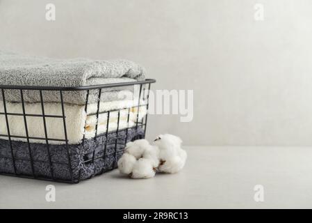 Pile de serviettes de bain avec fleurs de coton dans un panier en métal noir sur fond de béton clair Banque D'Images