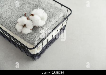 Pile de serviettes de bain avec fleurs de coton dans un panier en métal noir sur fond de béton clair Banque D'Images