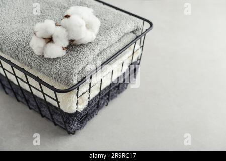 Pile de serviettes de bain avec fleurs de coton dans un panier en métal noir sur fond de béton clair Banque D'Images