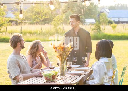 Délices du jardin : des amis multiraciaux s'unissent en soirée. Photo de haute qualité, découvrez l'enchantement d'une soirée de rassemblement dans un beau jardin, où un groupe multiracial d'amis se réunit pour un délicieux dîner et des moments de joie pure. Cette photographie captivante capture l'énergie vibrante et la chaleureuse camaraderie en s'asseyant autour d'une table, partageant des rires, des histoires, et un délicieux repas. Le cadre du jardin ajoute une touche de splendeur naturelle à la scène, créant un cadre parfait pour leurs conversations animées et leurs souvenirs précieux. Rejoignez ce groupe diversifié à mesure qu'il se présente Banque D'Images