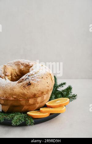 Petit gâteau maison décoré de poudre de sucre blanc, de limaces d'orange et de brindilles de sapin sur une assiette noire sur fond clair Banque D'Images