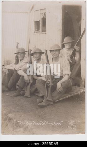 'Les chasseurs bolcheviques': Photographie de quatre soldats britanniques en casques Brodie avec carabines, assis à l'extérieur d'un bâtiment en fer ondulé, éventuellement une cabane de Nissen. La photo aura probablement été prise peu après la fin de la première Guerre mondiale, lorsque des soldats britanniques ont été envoyés en Russie pour intervenir dans la guerre civile russe Banque D'Images