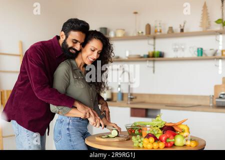 Amoureux des conjoints arabes cuisinant ensemble, heureux homme du Moyen-Orient aidant sa belle femme à couper des légumes, espace libre Banque D'Images