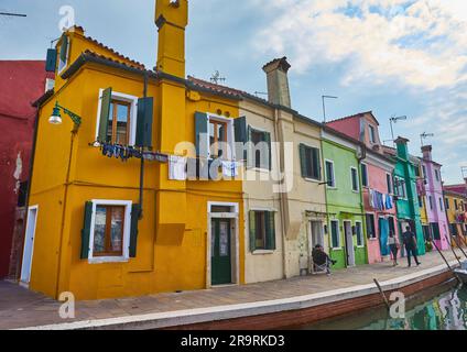 Île de Burano étroite rue pavée entre maisons colorées bâtiments avec murs lumineux multicolores, ciel bleu ensoleillé jour d'été, province de Venise, Banque D'Images