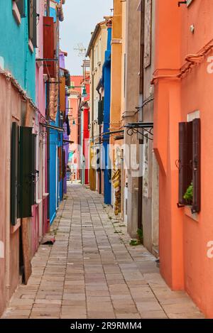 Île de Burano étroite rue pavée entre maisons colorées bâtiments avec murs lumineux multicolores, ciel bleu ensoleillé jour d'été, province de Venise, Banque D'Images