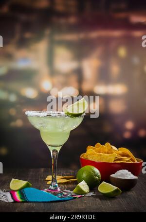 Cocktail de Margarita avec des limes entières et tranchées, nachos et sel sur une table de bar en bois. Ambiance de fête mexicaine Banque D'Images