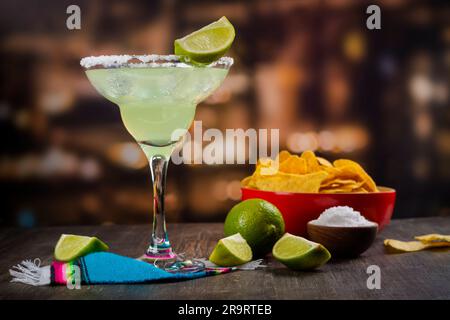 Cocktail de Margarita avec des limes entières et tranchées, nachos et sel sur une table de bar en bois. Ambiance de fête mexicaine Banque D'Images