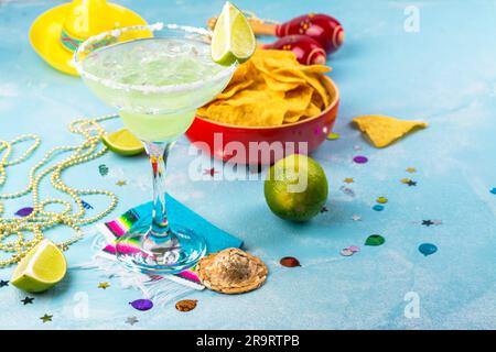 Cocktail de Margarita avec des limes entières et tranchées, nachos et sel sur table en pierre bleue. Ambiance de fête mexicaine Banque D'Images