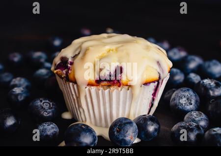 Vue rapprochée de Muffin aux myrtilles avec glaçage au citron : muffin aux myrtilles glacé dans un emballage en papier entouré de myrtilles fraîches Banque D'Images