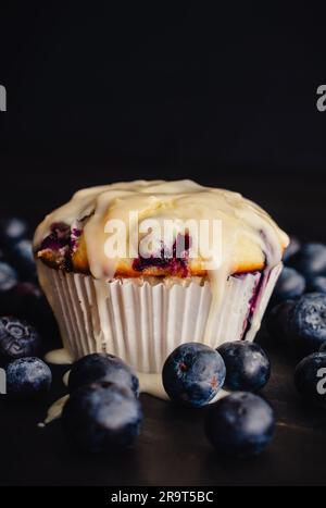 Vue rapprochée de Muffin aux myrtilles avec glaçage au citron : muffin aux myrtilles glacé dans un emballage en papier entouré de myrtilles fraîches Banque D'Images